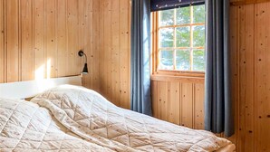 Quarto de cabana de madeira com cama, janela com cortinas e luminária na parede.