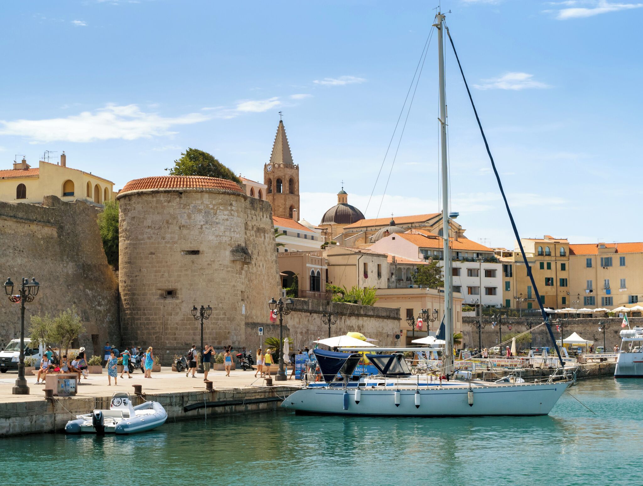 A coastal town with a historic fort, a church with a bell tower, and a marina with boats.