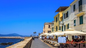 A seaside promenade with outdoor seating, a stone wall, and buildings with balconies. - Holiday apartment with air conditioning (Alghero)