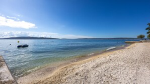 Une plage à l’eau claire, avec des galets et une côte visible au loin.