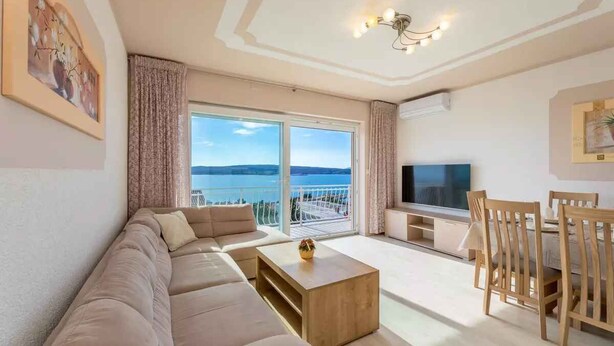 A modern living room with a large sofa, a coffee table, a TV, and a dining area with wooden chairs.