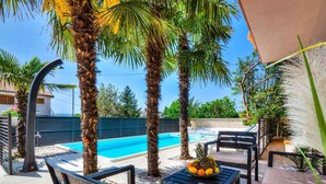 An outdoor pool area with palm trees, a table with fruits, and outdoor seating.