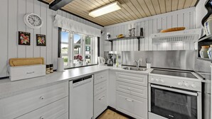 Una cocina moderna con armarios blancos, horno empotrado y una ventana con cortinas.