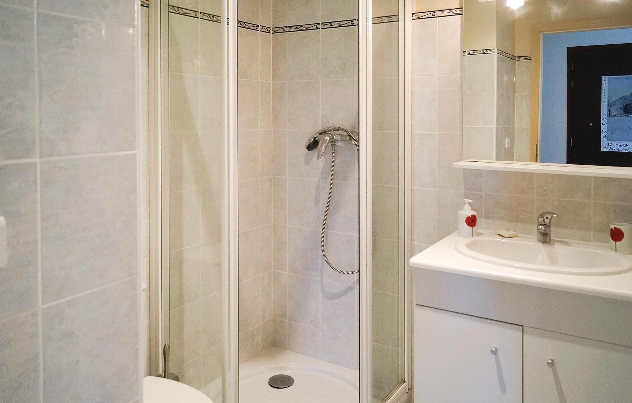 A modern bathroom with a glass-enclosed shower, a white sink with a mirror above it, and a small cabinet below.