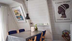 En matplats med ett rutigt bordsduksmönster, blå stolar, en hängande taklampa och väggdekorationer, inklusive en inramad affisch och en hylla med diverse föremål.