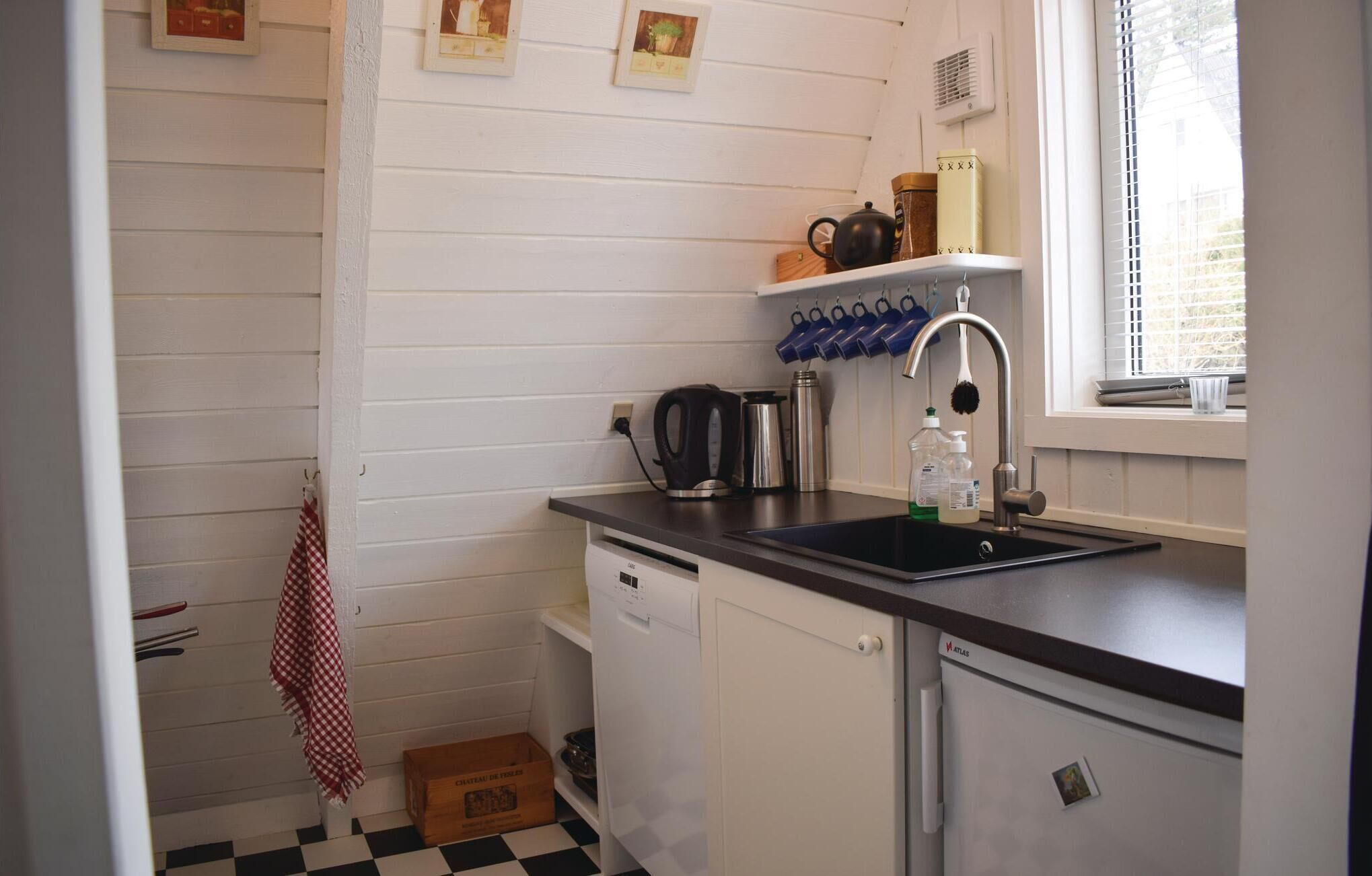 A compact kitchen with white cabinets, a black countertop, a sink, and a window with blinds.