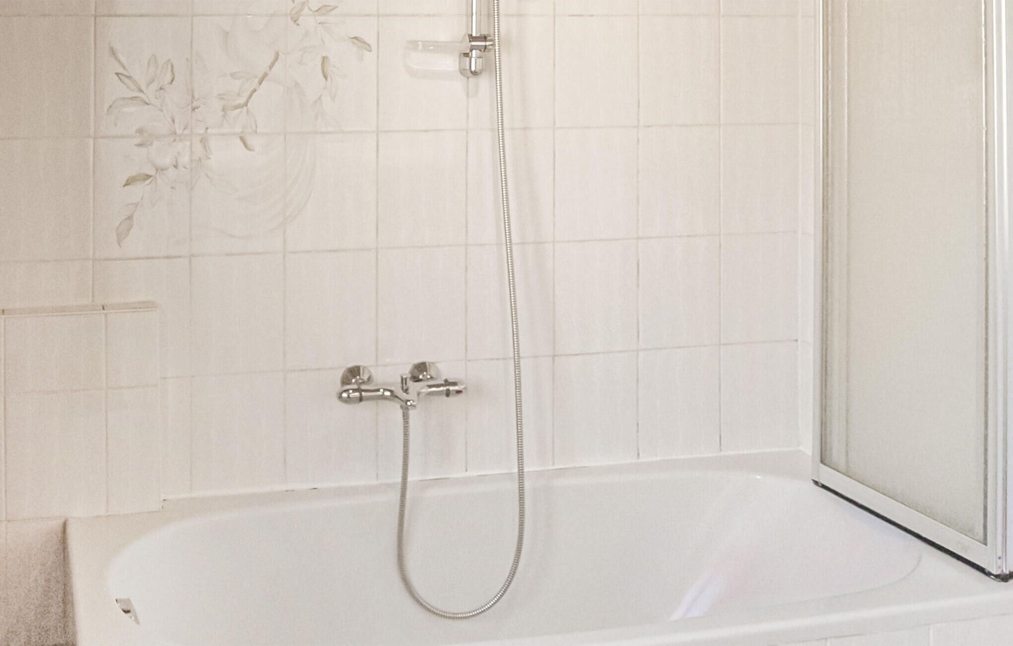 Une salle de bain avec une baignoire, une douche et un mur orné de carreaux à motifs floraux.