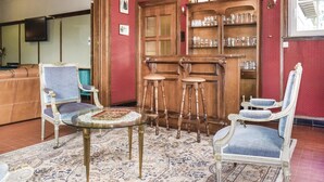 A room with a round glass table, two blue upholstered chairs, a wooden cabinet with glassware, and a red patterned wall.