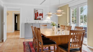 A dining area with a wooden table, chairs, a vase with flowers, and pendant lights.