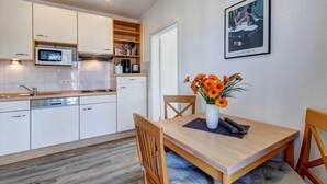 A modern kitchen with white cabinets, a microwave, and a coffee machine. There is a dining table with chairs and a vase of flowers. - Villa Aquamarina Whg. 26b, TERRACE, CAR CHAIR - Villa Aquamarina, 1st ROW, partly. (Heringsdorf)
