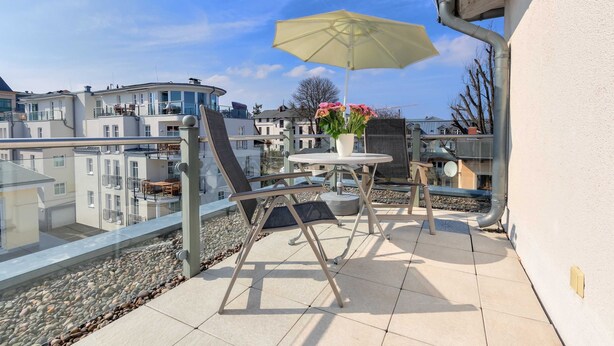 A balcony with a table and chairs, a yellow umbrella, and a vase with flowers. - Villa Aquamarina Whg. 26b, TERRACE, CAR CHAIR - Villa Aquamarina, 1st ROW, partly. (Heringsdorf)