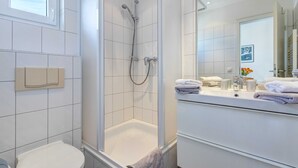 A modern bathroom with a glass-enclosed shower, a toilet, and a vanity with a mirror and towel rack. - Villa Aquamarina Whg. 26b, TERRACE, CAR CHAIR - Villa Aquamarina, 1st ROW, partly. (Heringsdorf)