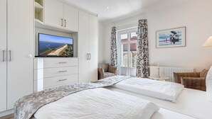 A hotel room with a large bed, a TV mounted on a cabinet, a window with patterned curtains, and a framed picture on the wall. - Villa Aquamarina Whg. 26b, TERRACE, CAR CHAIR - Villa Aquamarina, 1st ROW, partly. (Heringsdorf)