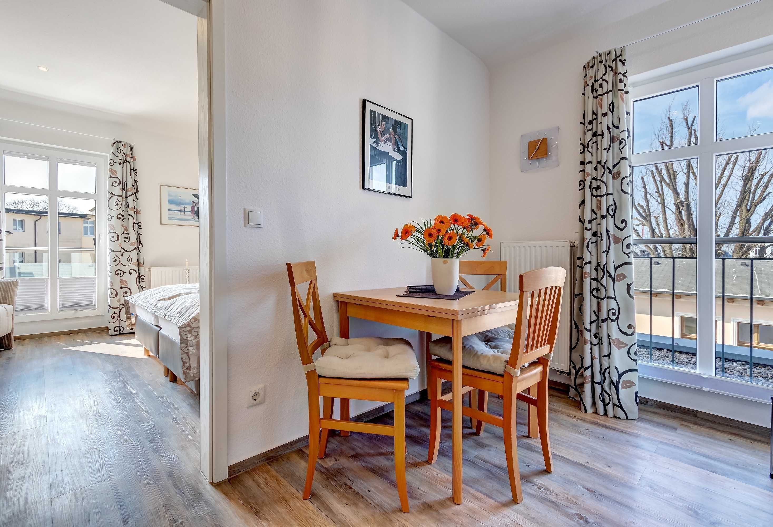 Un coin repas avec une table et des chaises en bois, un vase rempli de fleurs et un tableau encadré accroché au mur.