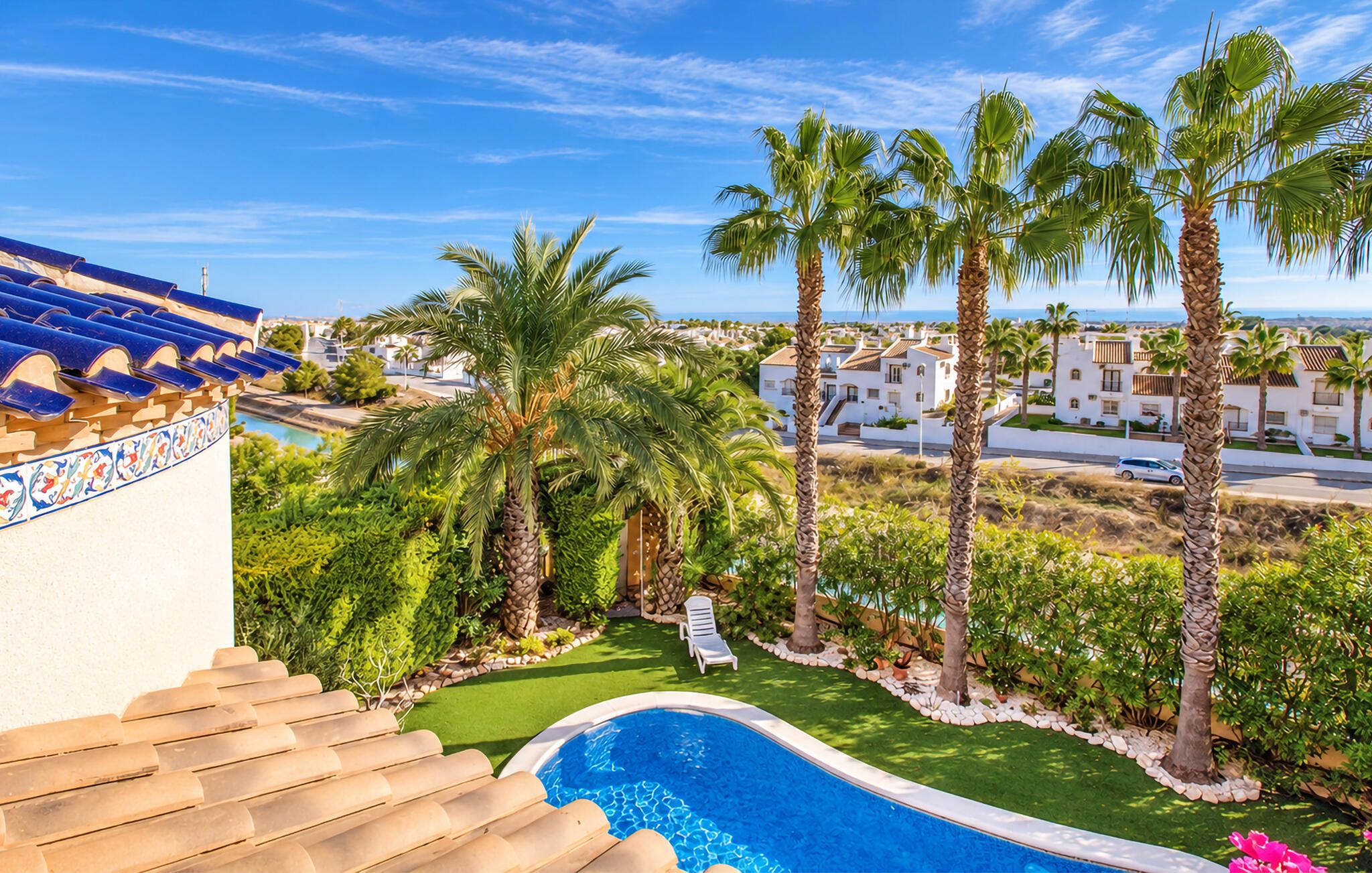 A swimming pool surrounded by palm trees and a view of a coastal town.