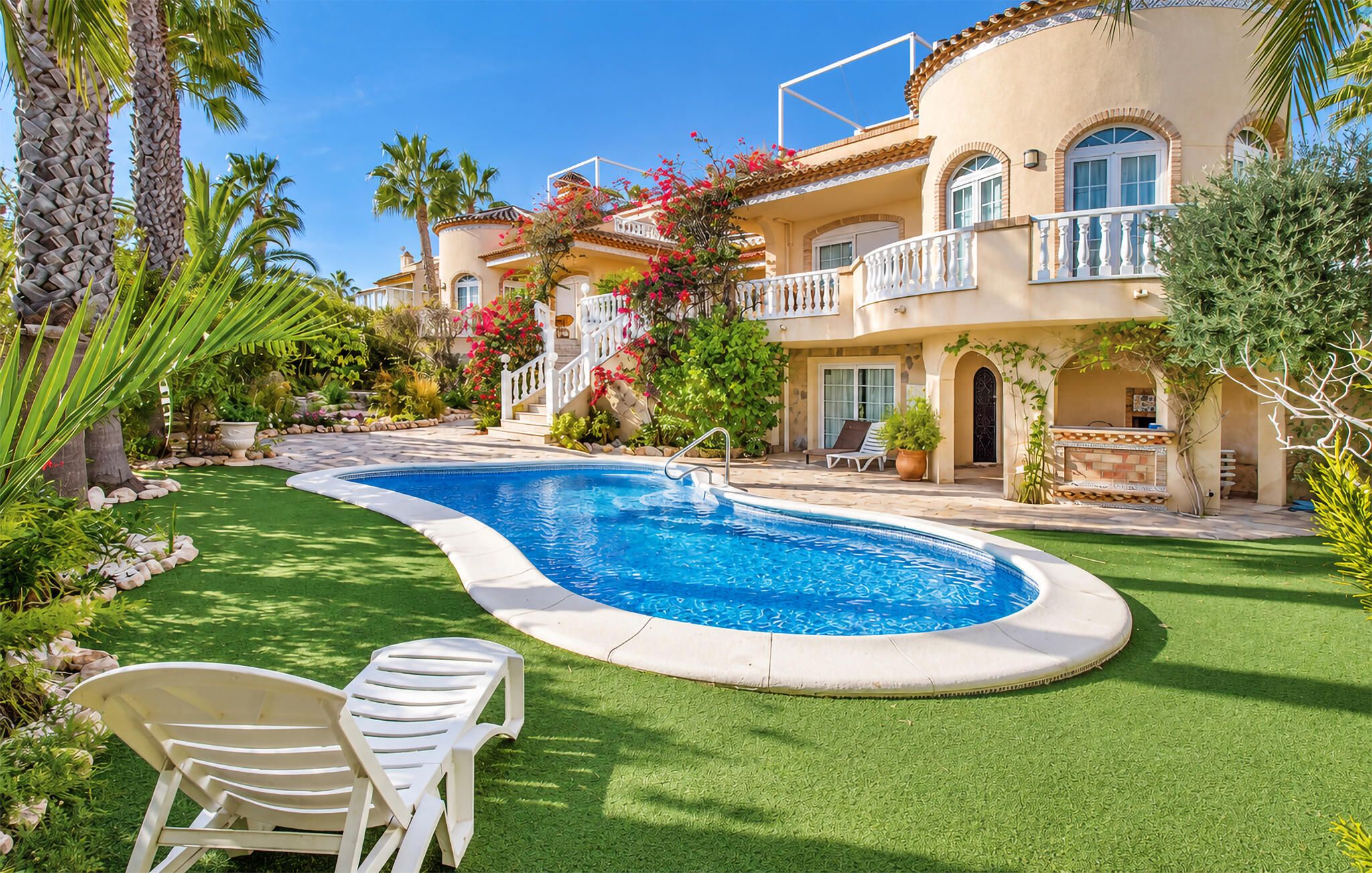 Ein Pool mit geschwungener Kante, umgeben von Kunstrasen und zwei weißen Liegestühlen.
