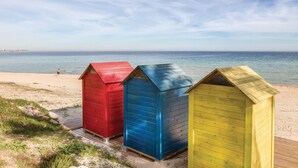 Drei Strandhütten an einem sandigen Strand, im Hintergrund das Meer.