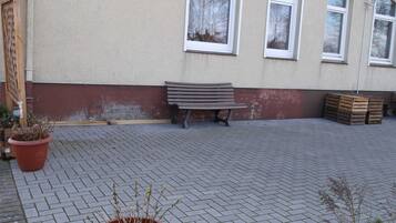 Ein gepflasterter Außenbereich mit einer Bank, Blumentöpfen und Holzkisten.