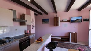 Une cuisine équipée d’une cuisinière, d’un évier et de placards. On y trouve un saladier rempli de fruits sur le comptoir et une chaise noire placée devant.
