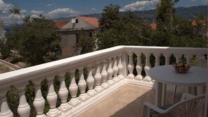 Un balcon avec une balustrade blanche, une table ronde entourée de chaises et un saladier rempli de fruits.
