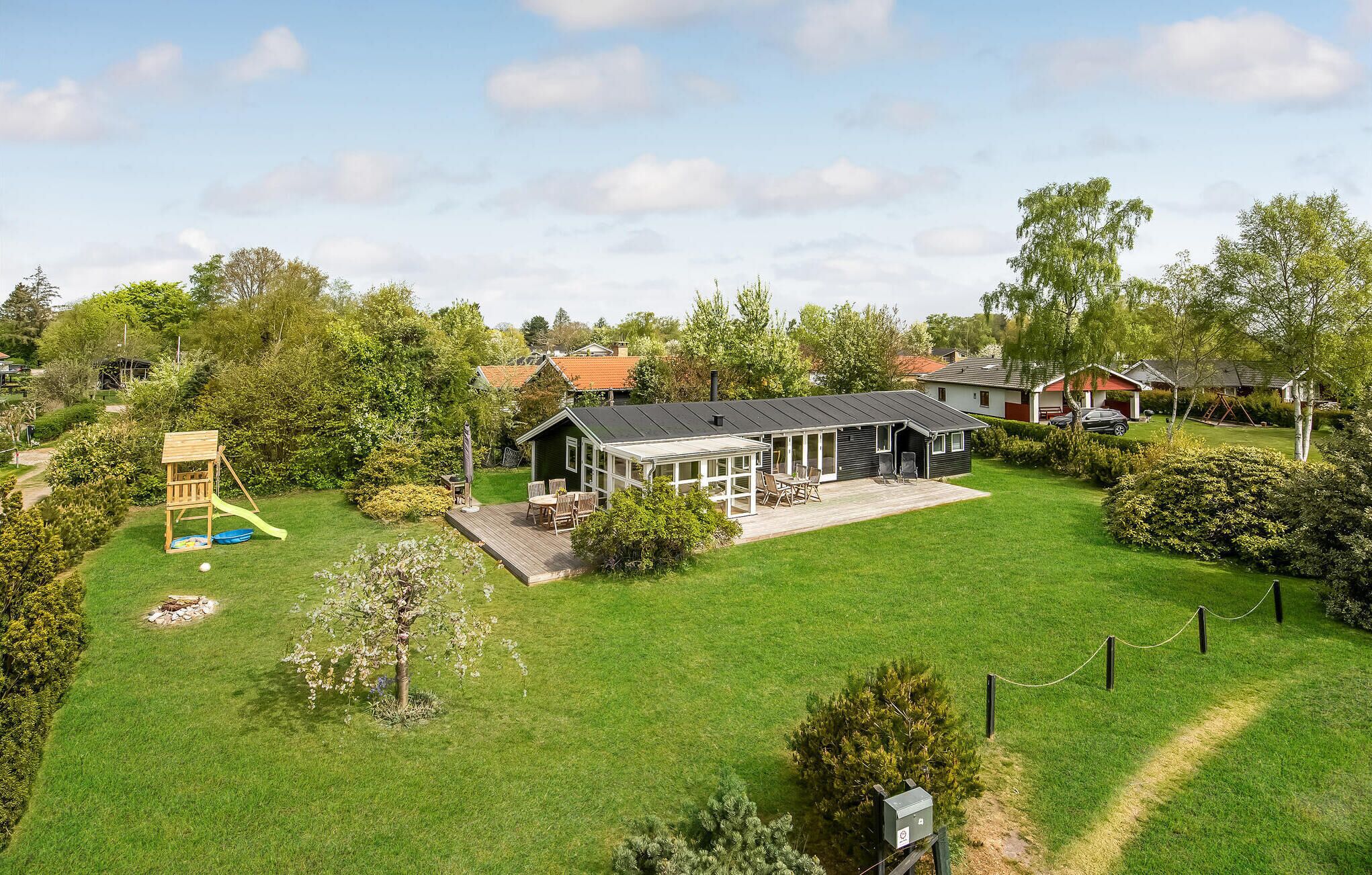 A residential property with a large lawn, a wooden play structure, a covered patio, and a house with a dark roof.