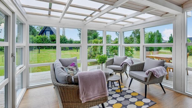 Ein Wintergarten mit Glasveranda, Korbmöbeln und Blick auf einen Garten.