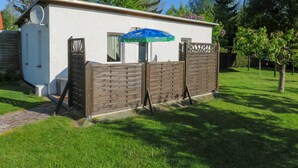 A small, single-story building with a white exterior, a wooden fence, and a blue umbrella. - Bungalow Alms, Germany (Ribnitz-Damgarten)