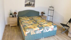 A bedroom with a bed, two bedside tables, a chair, a wall-mounted shelf, and a painting. - Bungalow Alms, Germany (Ribnitz-Damgarten)