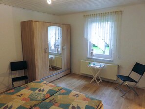 Quarto com cama, escrivaninha, cadeira, guarda-roupa e janela com cortinas.