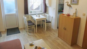 A compact room with a dining table, two chairs, a small cabinet, and a window with curtains. - Bungalow Alms, Germany (Ribnitz-Damgarten)