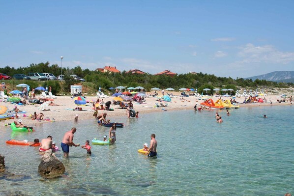 Una playa con agua cristalina, gente nadando y diversas actividades recreativas.