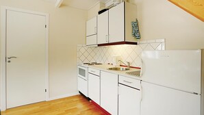 A compact kitchen with white cabinets, a built-in oven, a refrigerator, and a wooden ceiling. - 2 bedroom amazing apartment in Gudhjem (Gudhjem)