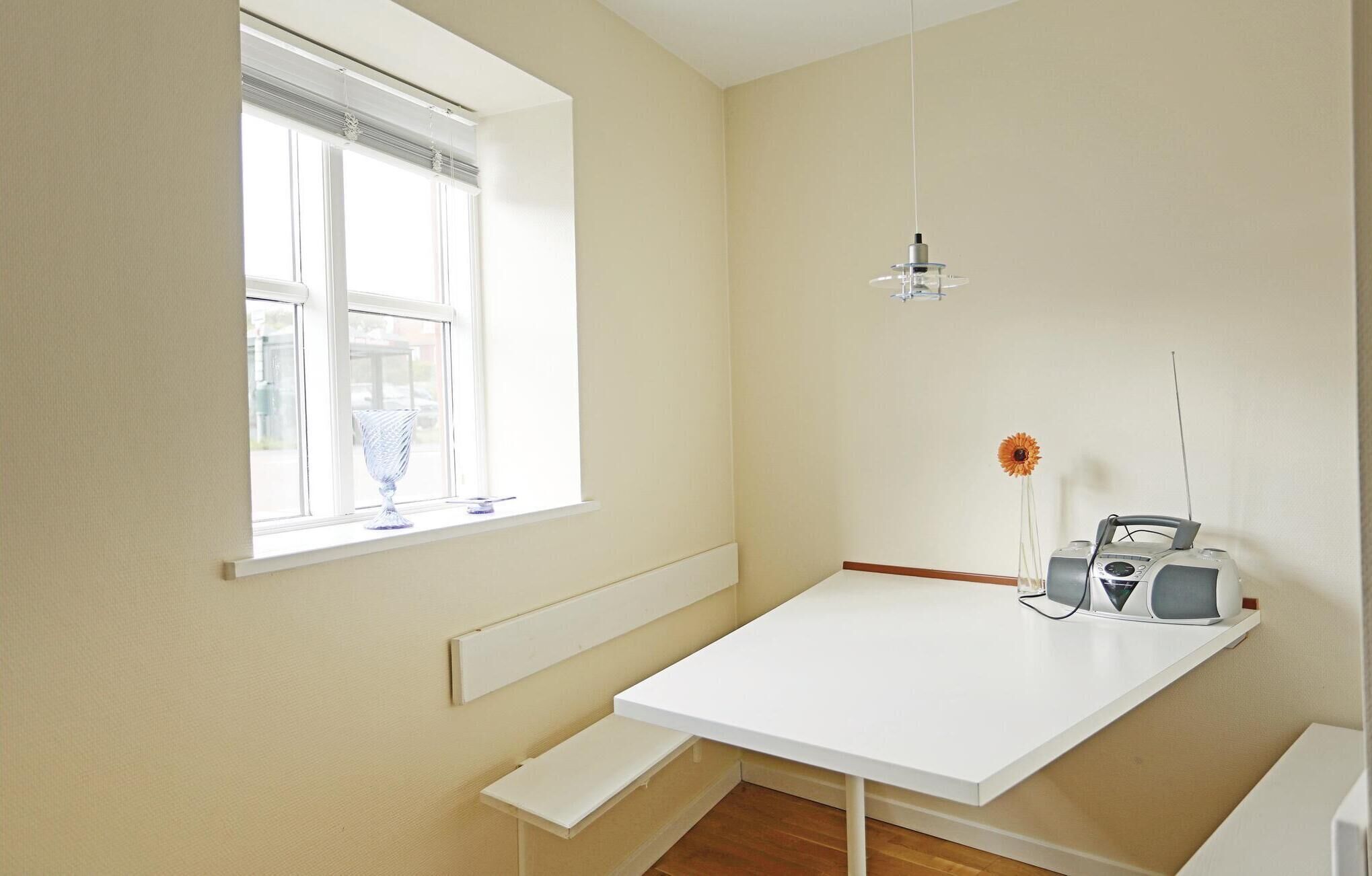 A small, bright room with a white table, a window with blinds, a hanging light, and a radio.