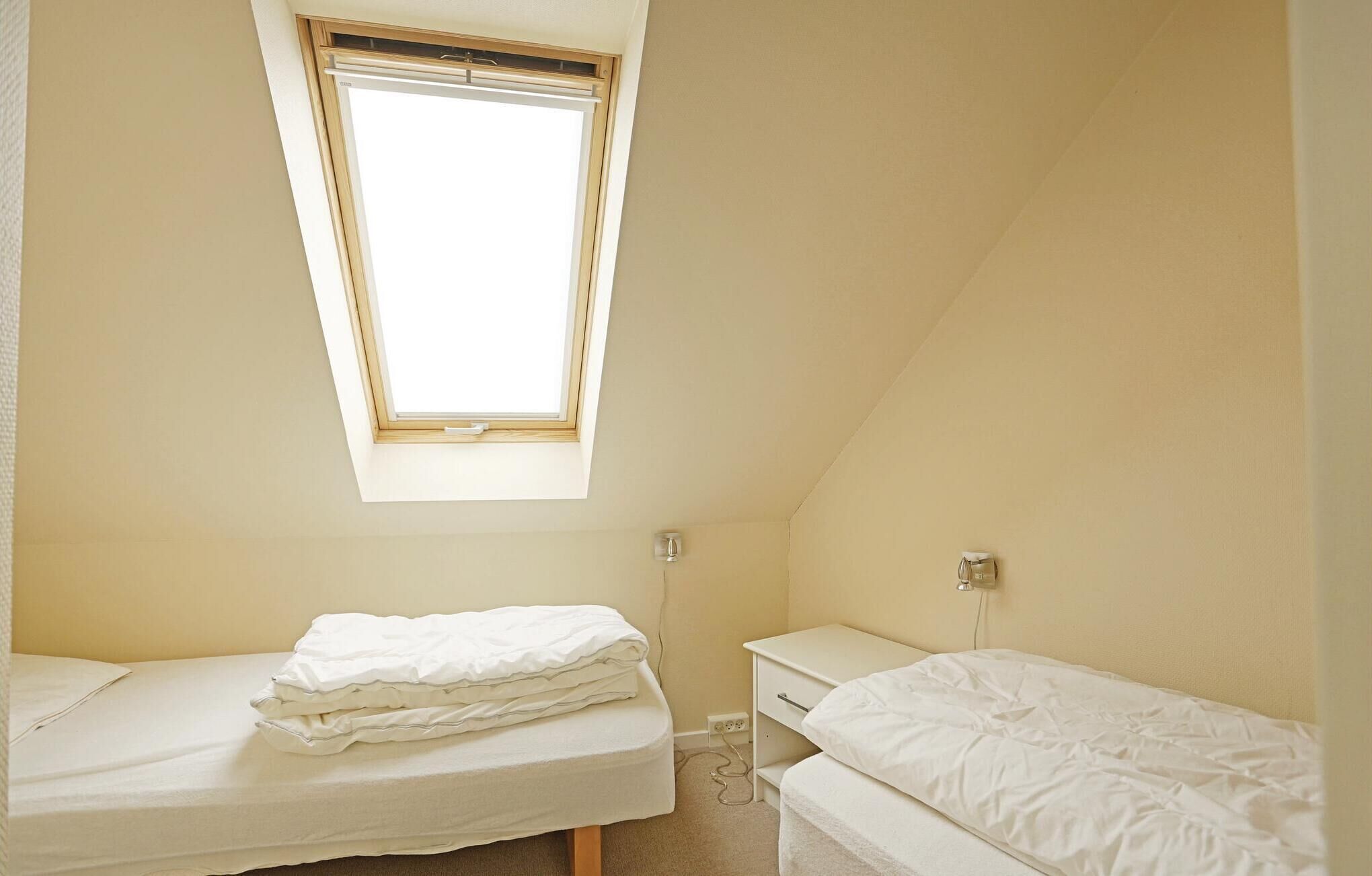 A small, single-bed room with a skylight, a bedside table, and a power outlet.