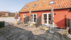 A red building with a tiled roof, outdoor seating with chairs and tables, and a fenced patio area. - 2 bedroom amazing apartment in Gudhjem (Gudhjem)