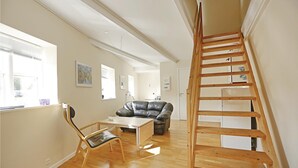 A spacious room with a wooden staircase, a leather sofa, a wooden dining table, and a chair. - 2 bedroom amazing apartment in Gudhjem (Gudhjem)