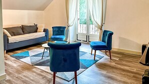 Una sala de estar con un sofá, dos sillones y una mesa de centro. Hay una ventana con cortinas, una puerta y vistas a zonas verdes.