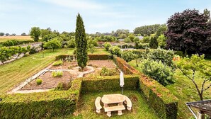 Un jardín con un banco de piedra, setos recortados y diversas especies de árboles.