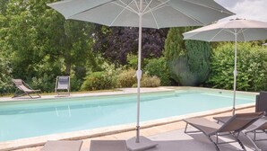 Piscina con sillas de descanso y sombrillas, rodeada de vegetación.