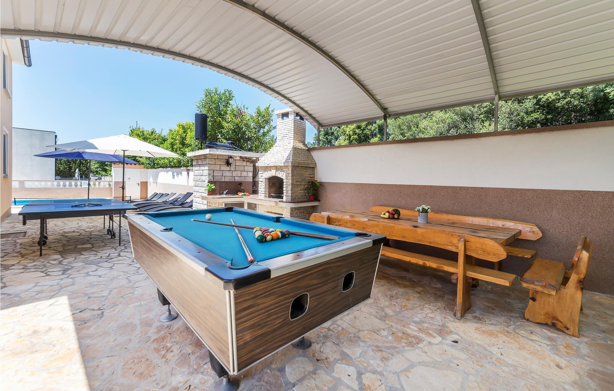 Ein Außenpoolbereich mit Pooltisch, Grill und Holzbank.
