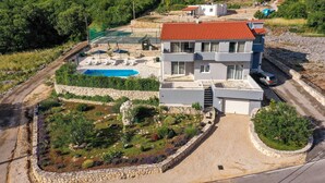Une maison moderne à deux étages, dotée d’une piscine, entourée de jardins aménagés et d’un mur en pierre.