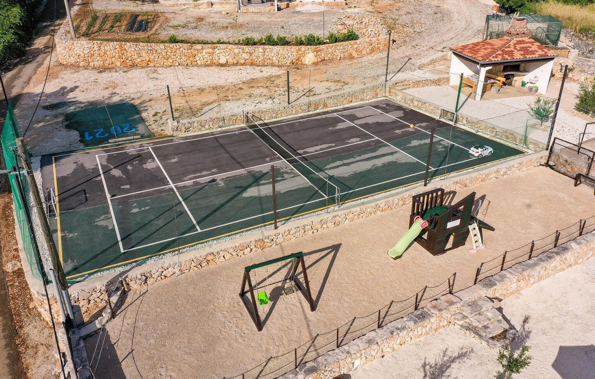 En utomhusbana för tennis med nät, omgiven av en stenmur och ett inhägnat område.