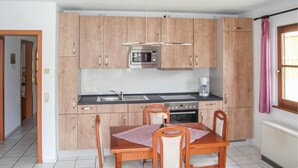 Una cocina con armarios de madera, microondas, cafetera y una mesa de comedor con sillas.