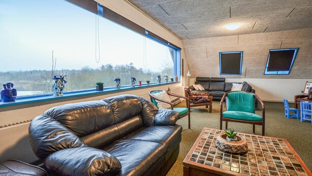 Una sala de estar acogedora con un ventanal grande, un sofá de cuero, un sillón verde y una mesa de centro con una planta.