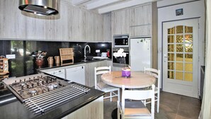 Une cuisine moderne équipée d’une cuisinière à gaz, d’un évier et d’un réfrigérateur. On y trouve une table à manger avec des chaises, ainsi qu’un petit objet décoratif posé dessus.