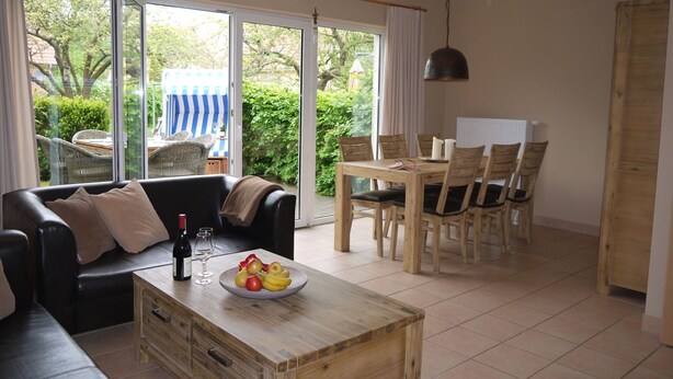 A modern living room with a sofa, a wooden coffee table with fruit, and a dining area with a table and chairs. - Cottage Riedensee (Kühlungsborn)