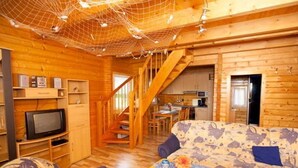 A wooden cabin interior with a sofa, television, kitchen area, and a staircase. - Ferienhaus Kranichblick am Bodden (Saal)
