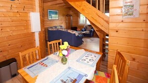 A wooden cabin interior with a dining table, chairs, a clock, a sofa, and a staircase. - Ferienhaus Kranichblick am Bodden (Saal)
