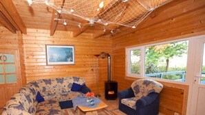 A cozy cabin interior with a wooden floor, two patterned sofas, a small table, and a large window. - Ferienhaus Kranichblick am Bodden (Saal)