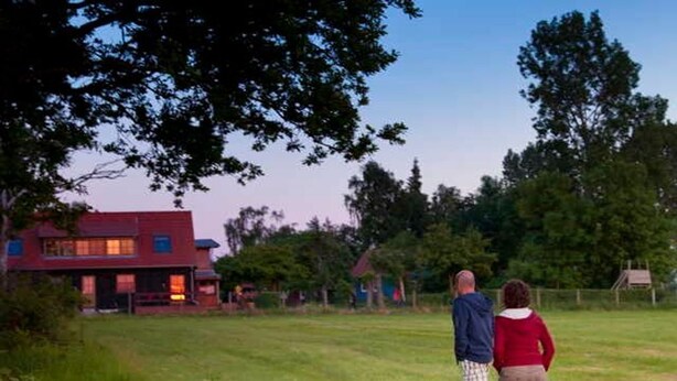 A grassy field with a red house in the background. - Ferienhaus Kranichblick am Bodden (Saal)